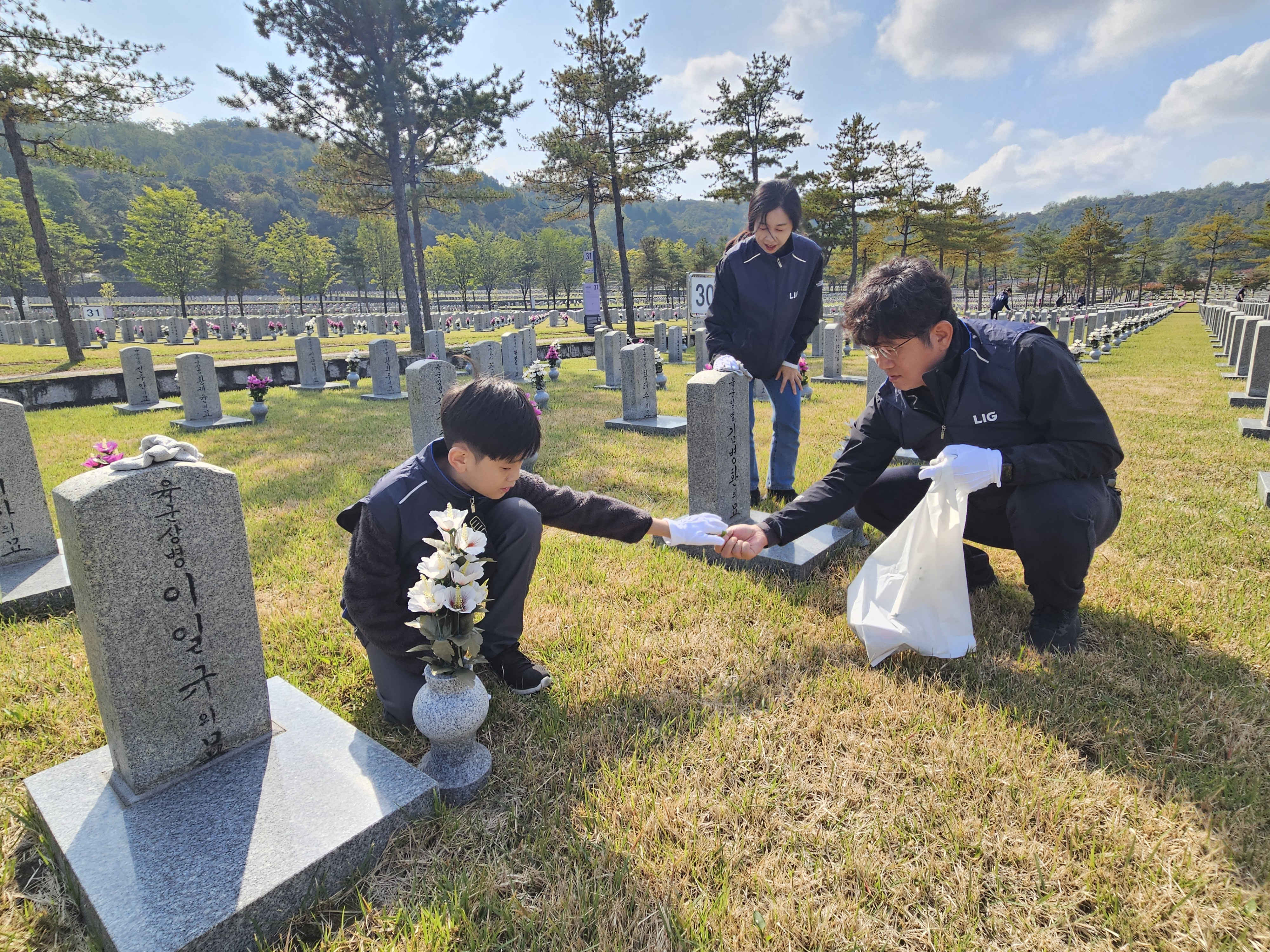 LIG넥스원 직원 가족이 25일 국립서울현충원 30묘역에서 묘역 단장 봉사활동을 펼치고 있다. 사진=LIG넥스원