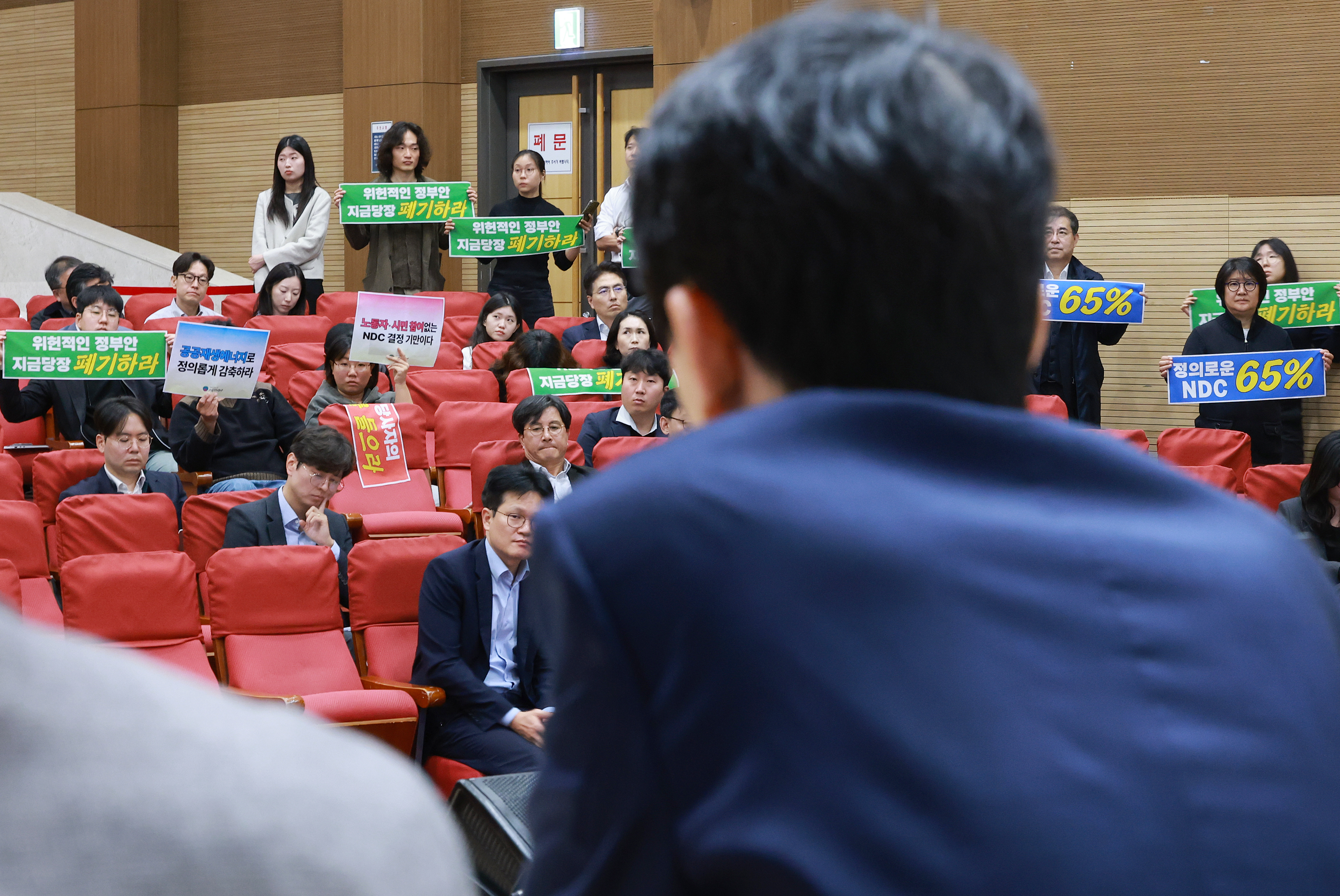 서울 여의도 국회 의원회관에서 열린 2035 NDC 대국민 공개 논의 공청회에서 안세창 기후에너지환경부 기후에너지정책실장이 발언하는 가운데 참석자들이 정부안에 반대한다는 내용을 담은 손팻말을 들고 있다. 사진=연합뉴스