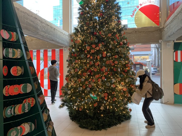 카카오뱅크 ‘Holiday in 모임아지트’에서 한 방문객이 ‘모임 위시 트리’에 새해 소망이 담긴 오너먼트 종이를 달고 있다. 사진=강예슬 기자