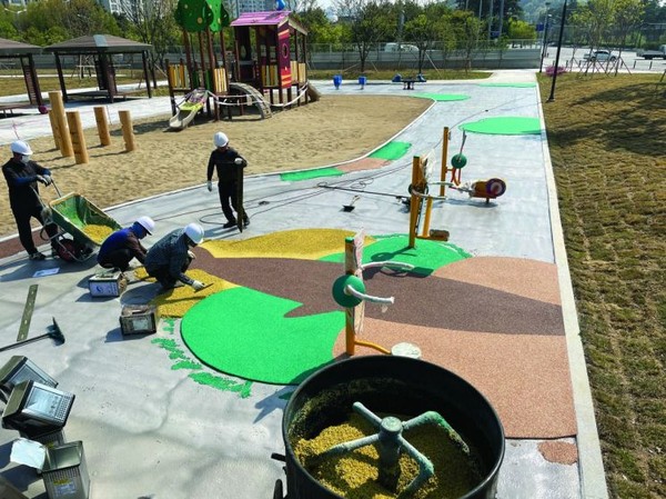 근로자들이 중소기업 인증 자재를 이용해 놀이터 바닥을 우레탄으로 시공하고 있다.